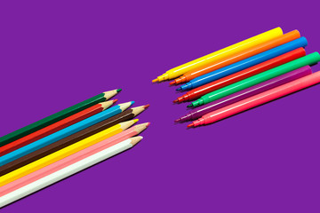 colored pencils lying against felt pens on a purple background. concept of office and educational chancery. free space for advertising text