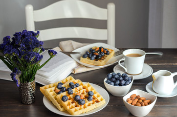 Obraz na płótnie Canvas Belgian waffle decorated with blueberries and nuts, open book on wooden table for perfect breakfast at Sunday. Homemade dessert background. Relax moments concept.