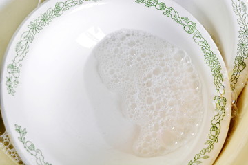 wash dirty dishes: dish with a pattern and blue sponge in soapy water in the kitchen sink