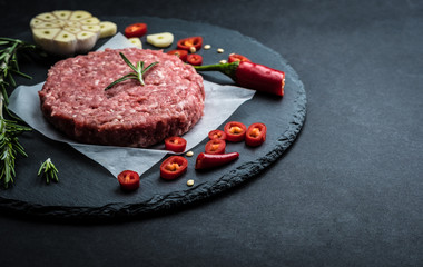Raw ground beef meat burger steak cutlet with chili, rosemary and garlic on black slate plate for cooking