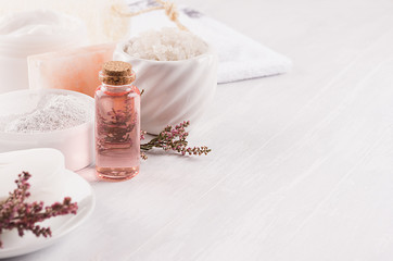 Gentle pink cosmetics oil, small flowers and white soap, cream, clay, towel closeup on white wooden background, copy space.