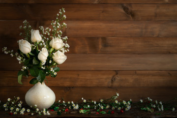 still life of white rose with small white daisy in a vase on wooden plank with wooden background