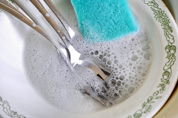 wash dirty dishes: forks and plates with a pattern with a sponge in soapy water in the kitchen sink