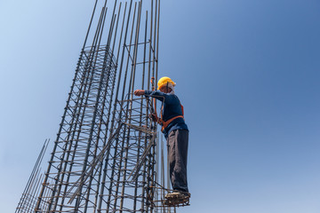 worker at altitude strengthens the pillars from rebar, on the blue sky background. candid, real people