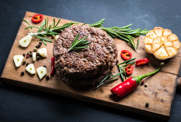Delicious beef burger steak with spices and herbs on cutting board and slate background, top view