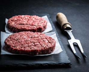 Raw minced meat ground beef burger cutlet with carving fork prepared for grilling on cooking slate