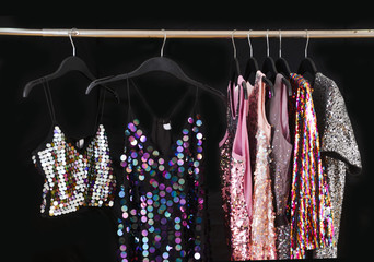 Row of vest with sequins colorful sundress hanging on hanger– black background, 