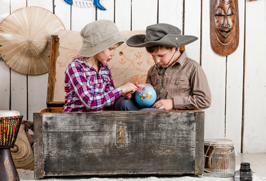 little boy and girl study globe sitting in big old chest