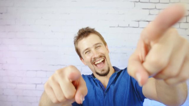 Man mocking you in slow motion 4K. Portrait of a male person in focus pointing fingers towards the camera. Bricks background wall with side colorful light.