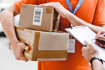 A person wearing an orange T-shirt and a name tag is delivering a parcel to a client, who is...
