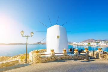 Obraz premium Old white windmill on the cliff in front of water and beautiful blue sky at sunny day, Paros, Greece