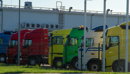 Trucks are parked near a production warehouse. Trucks truckers are on the TIR parking lot. Multicolored truck cabins near warehouses. Cargo transportation by trucks. Parking for truck drivers.