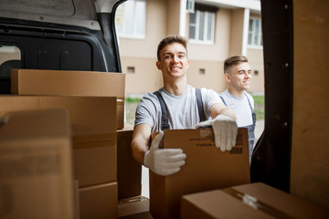 Two young handsome workers wearing uniforms are standing next to the van full of boxes. House move,...