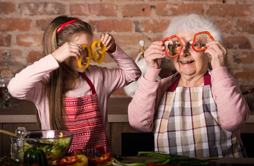 Grandchild with granny holding slices of bell pepper in front of their eyes smiling