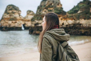A young woman tourist with a backpack enjoys the beautiful views of the Atlantic Ocean and the landscape off the coast in Portugal.