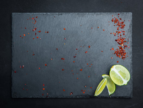 Gray textured board with laim and pepper on the dark background