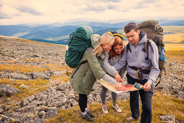 A team of travelers from two women and men with backpacks orient themselves to the terrain, study maps and navigate the route through the mountains. Travel Lifestyle and survival concept rear view.