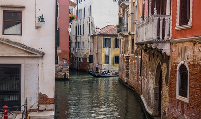 Obraz na płótnie Canvas Beautiful old venetian narrow street with old shabby colorful buildings. Gondolier with paddle in his hands rides a gondola with tourists.