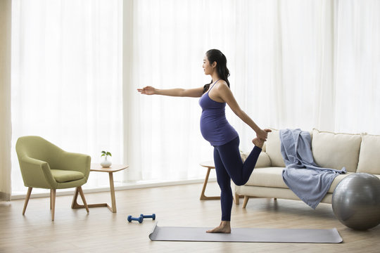 Cheerful pregnant woman practicing yoga at home