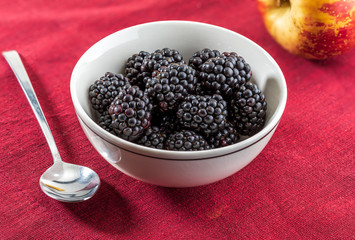 Delicious fresh blackberries and ripe black and reddish garnet. In white bowl on red and white background. With and red apple.