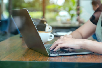 Closeup image of a woman working and typing on laptop keyboard with coffee cup on the table