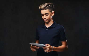 Handsome young guy dressed in a black t-shirt using a tablet computer. Isolated on a dark background.
