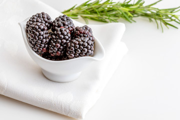 Delicious fresh blackberries and ripe black and reddish garnet. In white bowl and isolated background. With lavender, rosemary, lemon zest, mint and apricots.