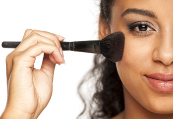 portrait of a young dark-skinned woman applying blush with brush on a white background
