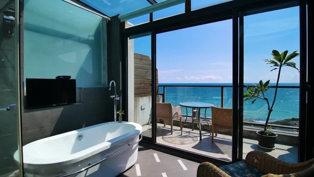 Beautiful Sea view Bathroom Interior Track Shot. Luxury sea view bathroom interior. Balcony with beautiful blue sky and sea view with chairs and table outside a luxury bathroom with glass ceiling. 