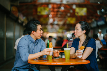 Portrait of a Chinese Asian couple enjoying their snack consisting of sugarcane juice and fried bananas at a hawker center during the weekend in Singapore, Asia.