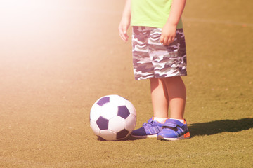 Kid's feet and soccer ball on green field