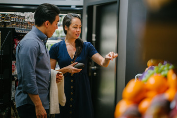 A young and happy Asian Chinese couple doing shopping together in a supermarket. Both are smiling while doing their shopping.
