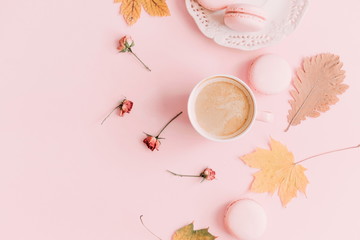 Autumn trendy composition. Cup of coffee and macaroon, dry leaves and flowers on pastel pink background. Flat lay, top view, copy space 
