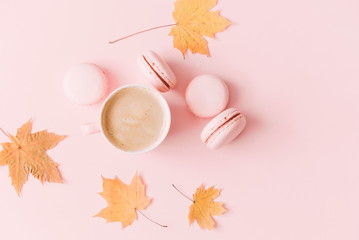 Autumn trendy composition. Cup of coffee and macaroon, dry leaves and flowers on pastel pink...