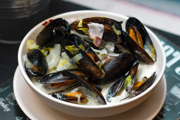Mussels with onions and bacon in cream sauce in deep plate on the table