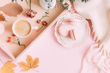 Autumn home cozy composition. Cup of coffee and macaroon, warm knitted plaid, yellow leaves and flowers on a light pink pastel background. Flat lay, top view, copy space 
