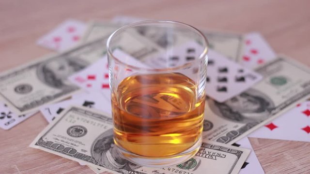 Glass of whisky over playing cards and dollar banknotes