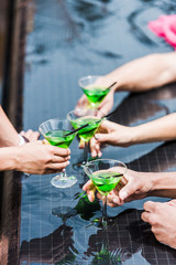 cropped image of friends clinking glasses with cocktails near swimming pool