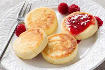 Obraz na płótnie Canvas Cottage cheese pancakes or syrniki with raspberry jam on white plate, closeup view. Russian, Ukrainian cuisine. Healthy tasty breakfast