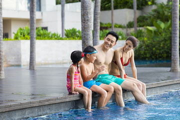 Happy young family sitting side by side at the pool