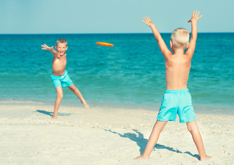 Brothers play with frisbee on the beach. Summer holidays.