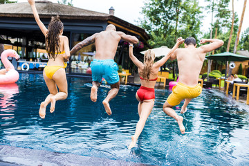 rear view of young friends having fun and jumping into swimming pool