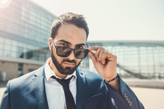 Bearded businessman wears blue suit and sunglassesbefore modern building