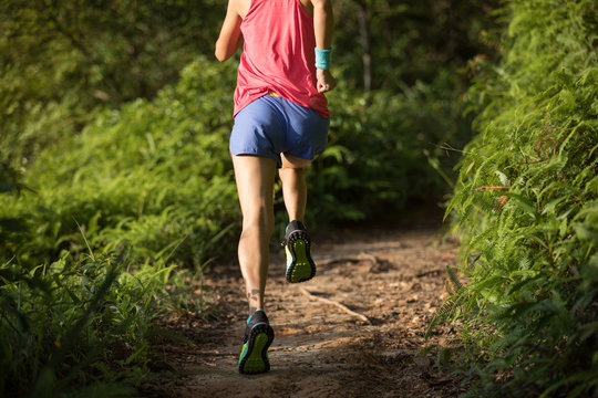 Fit woman trail runner running in morning forest