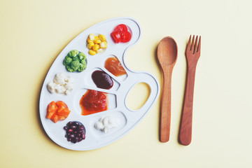 white palette with tasty colorful vegetables and sauces and wooden cutlery on yellow background,...