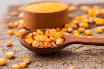 a bowl of corn is on a wooden table.Wooden spoon of grains of corn.Grains of corn