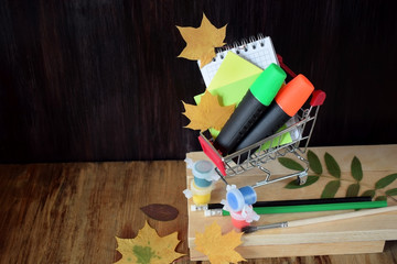 Notebook, stickers, highlighters in a shopping cart. Paints, brushes, pencils and autumn leaves...