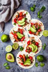 Mexican grilled chicken tacos with avocado, tomato, onion on rustic stone table. Recipe for Cinco de Mayo party. Top view, overhead, flat lay.