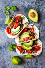 Mexican grilled chicken tacos with avocado, tomato, onion on rustic stone table. Recipe for Cinco de Mayo party. Top view, overhead, flat lay.