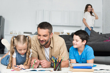 selective focus of father helping kids with homework while woman talking on smartphone at home